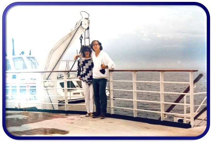 Two women standing together on a ship deck beside the sea